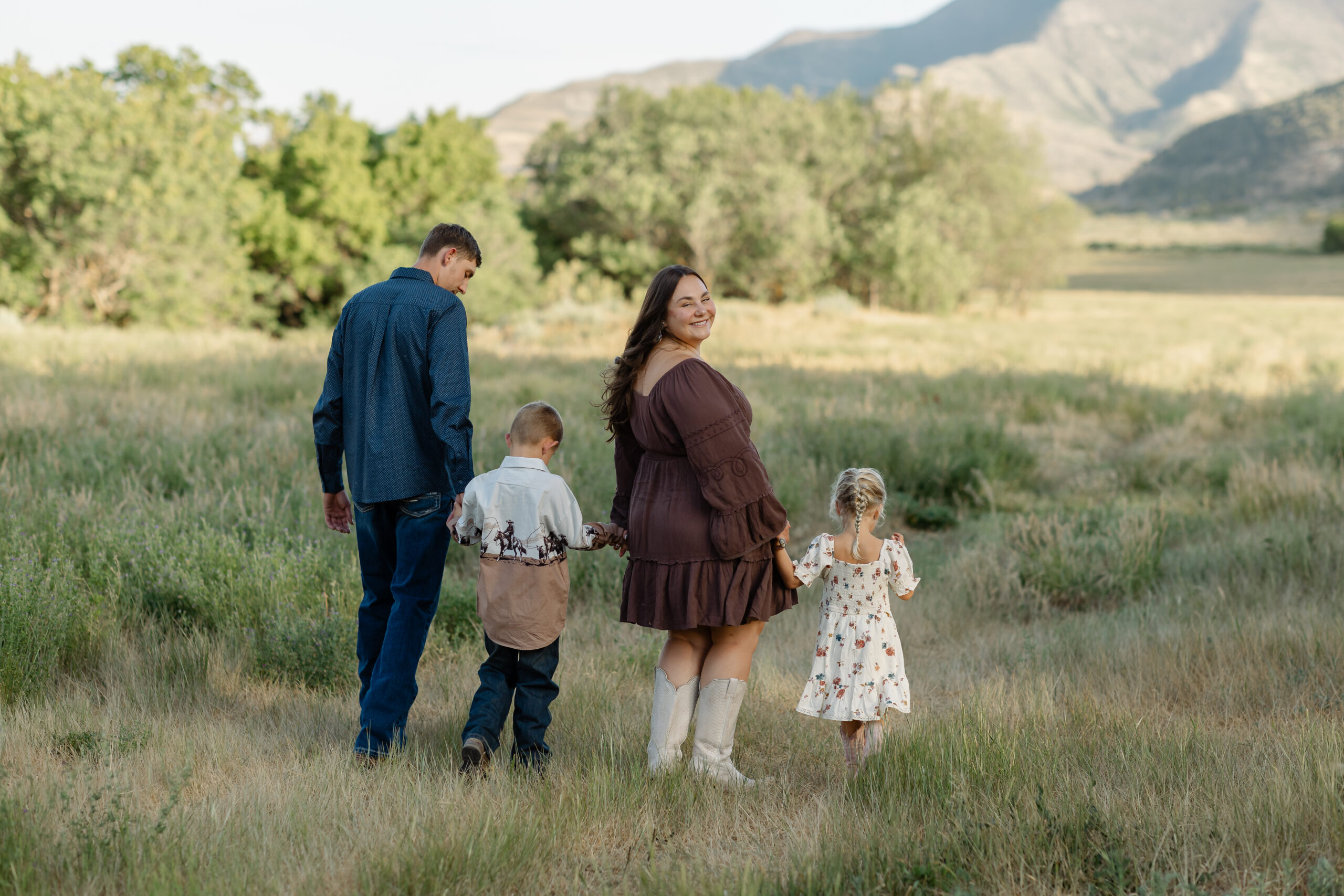 Family of four walking hand in hand through a grassy field with Colorado mountains in the background during a family photography session
