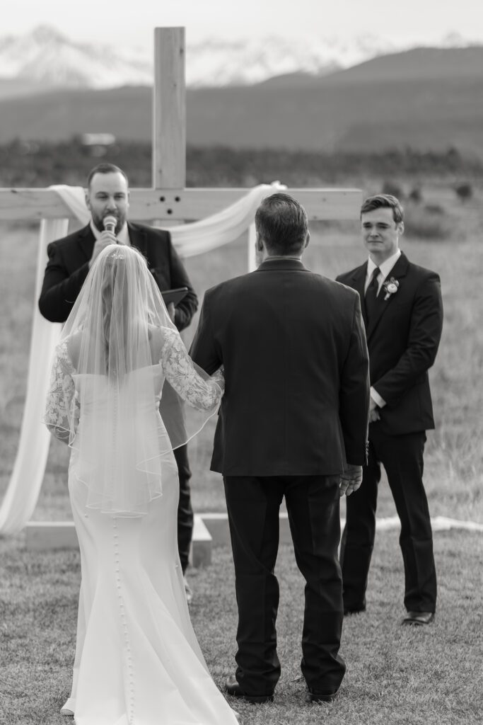 Bride standing with her father at the end of the aisle as the groom looks at her during their Colorado wedding ceremony